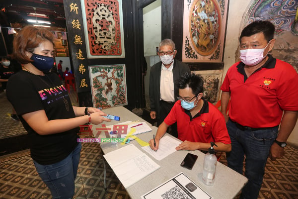 李斯斌（坐者）协助民众登记接种疫苗，站者右起为林千宏及史亚狮。