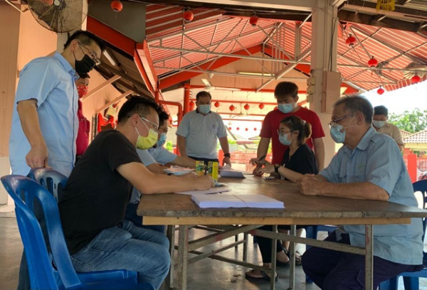 林万锋（站者）视察在柏淡芙露新村，进行的马华协助疫苗接种登记活动。左为蔡求伟协助年长村民填写表格。