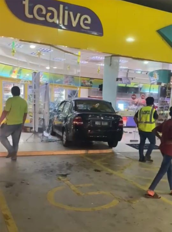 商人在油站添油后，准备驱车离开时疑误踩油门，导致轿车直撞便利店玻璃门。