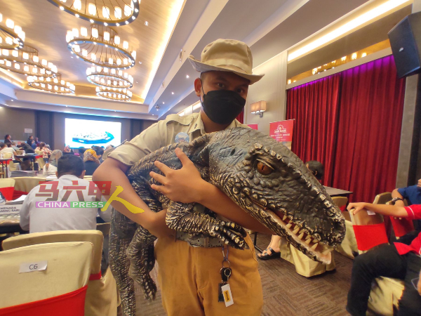 马六甲动物园员工抱着“恐龙”，向大家宣传恐龙公园。