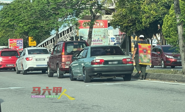 小贩在马六甲仙特拉巴士总站附近十字路口红绿灯，身上架着广告牌，贩卖食物。