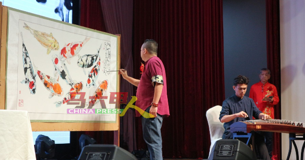 郭佳安（左）在《九鲤图》题字，由音乐老师陈劲隆伴奏。