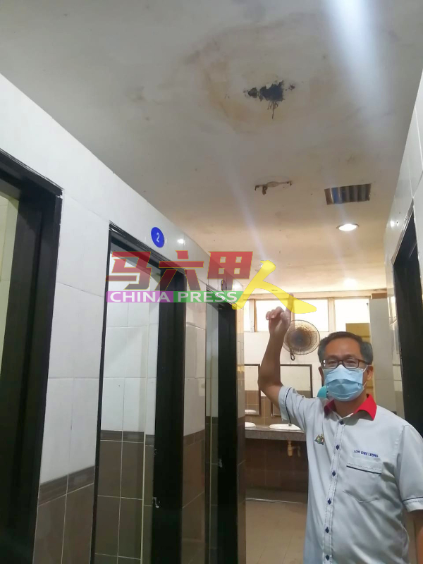 刘志俍查看发霉、漏水的公厕石膏天花板。