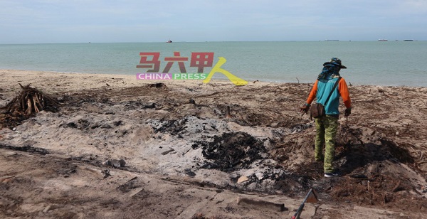 清洁工人清理留在沙滩上的焚烧垃圾和树根。