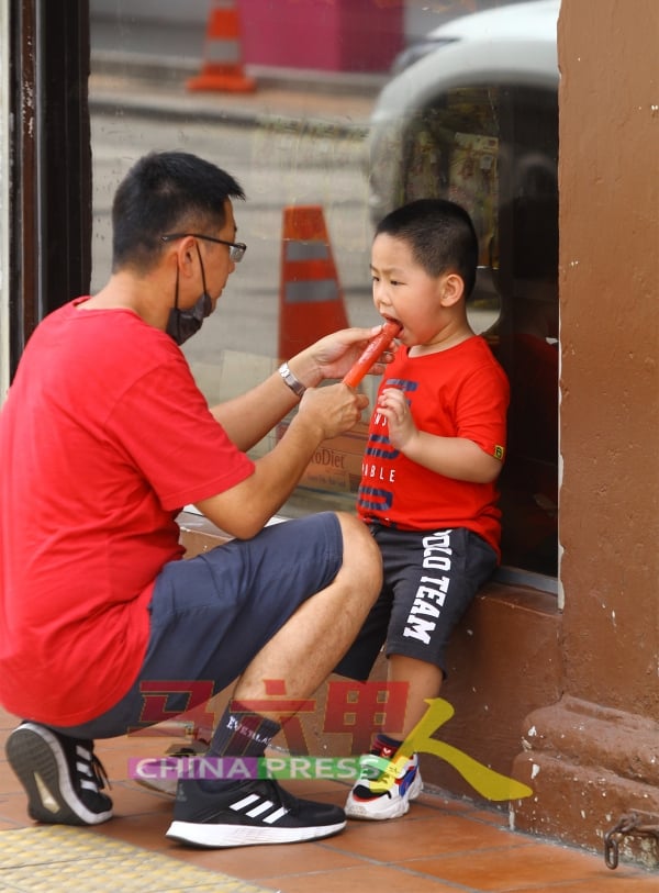 家长喂孩子食冰棒解暑。