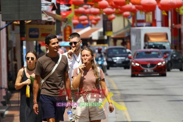 外国游客边逛街边享用冰淇淋，从中感受古城的炎热天气。