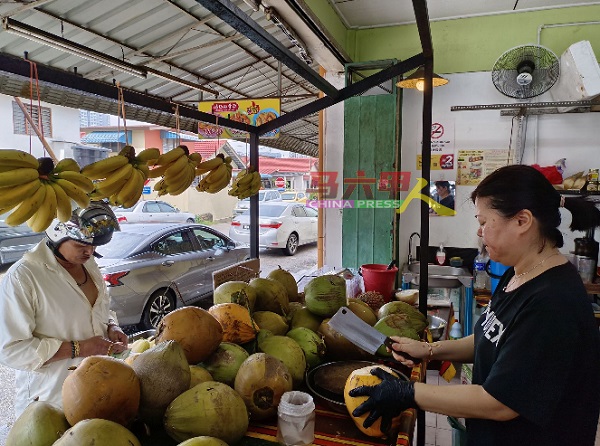 陈秋凤（右）协助顾客剥椰，把椰水、椰肉放进纸袋，方便顾客打包带走。