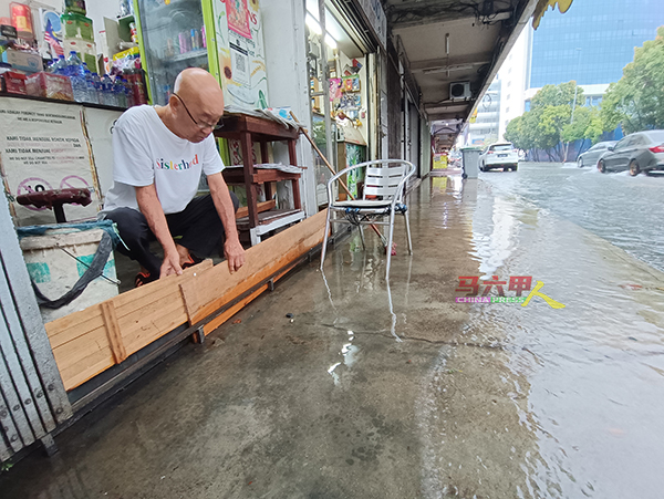 水灾来袭，民众赶紧使用板块围起门栏，避免雨水淹入店内。