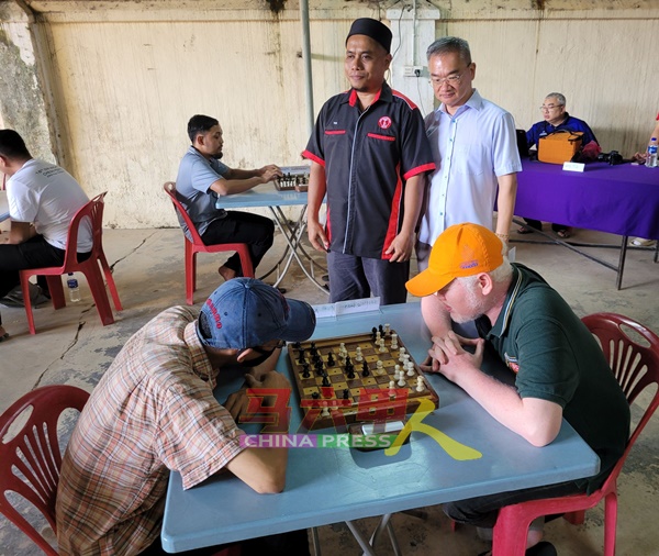 邱培栋（站者右起）在尤沙兹鲁陪同下，观看参赛者下棋。