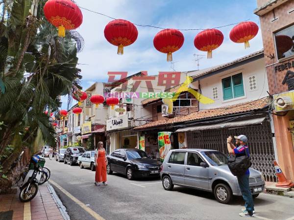 游客趁着无车辆经过，站在老街中与挂满红灯笼的老街合影。