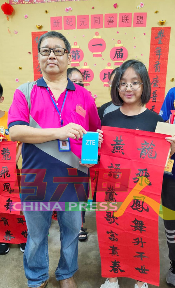 邓福强（左）代表陈水祥颁赠一台手机予中学组特优奖得主李恩希。