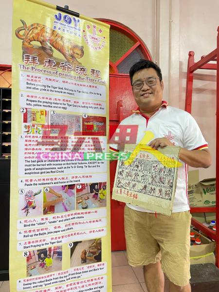 雷宝权向《中国报》展示马六甲保安宫打造的拜虎爷流程条幅，以及过去多年采用的白色吉纸（虎爷纸）。