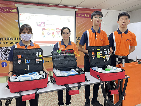 莫萃萱（左起）、郑伊婷、峇章慈善基金救伤队少年组主席佘惟义及陈玺安，一起教导青少年学员认识急救箱。