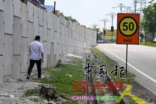 郭子毅沿着大路旁空地走向前，以视察围墙导致大道路面变窄情况。