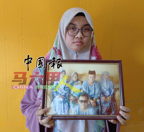 阿妮莎一脸哀伤地向在场的记者展示家庭照，照片中，弟弟开心地与双亲及两名姐姐合照。