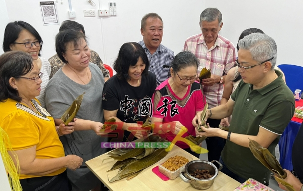 许金汉 (右) 在妇女组成员的指点下，成功包里并蒸煮出香喷喷的粽子。