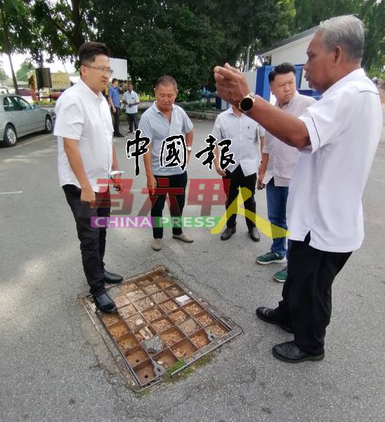 谢守钦（左）查看警局前的松弛路面铁盖。