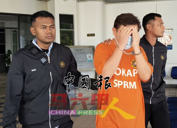 反贪污委员会执法员把华裔业务董事(中)押上法庭申请延长扣留令。