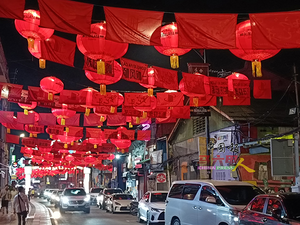 夜晚的鸡场街上空悬挂着2025盏灯笼和多条红布条，象征喜庆与好运，营造浓浓的节庆氛围。