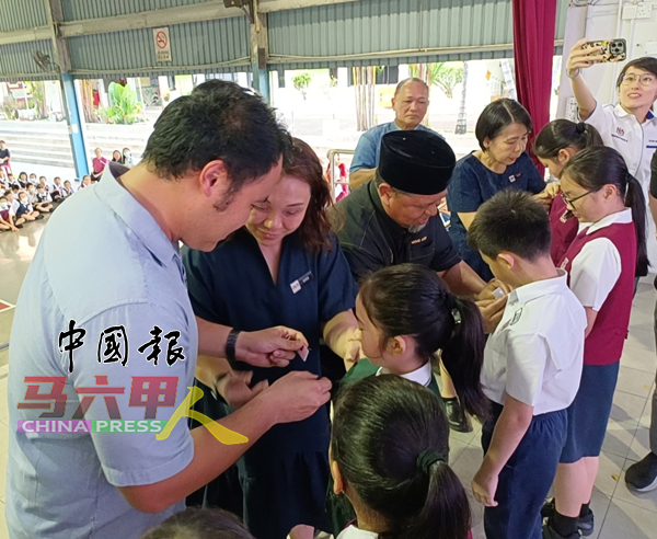 ■郭子毅(左起)在副校长周书均协助下,为学生佩戴国旗扣章。