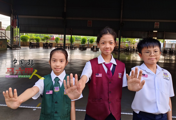 爱小学生诗佳乐（左起）、郑奕绚及黄铂竣开心地佩戴国旗扣章，并展示昌明大马手势。