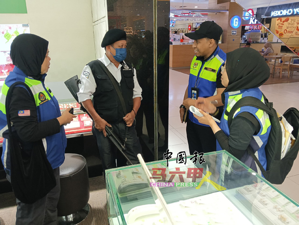 ■执法人员向一名持枪的金店保安员，了解工作时长和收入待遇。