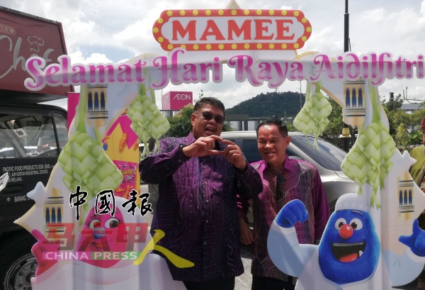 首长阿都拉勿（左）在Mamee美食摊前比爱心手势。右是朱国升。