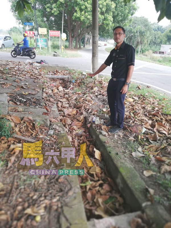李翰霖查看堵满干枯树叶的水沟。